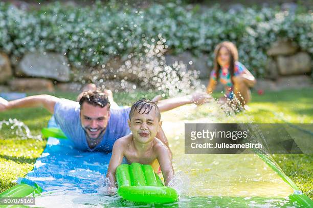family in garden playing water games - hose stock pictures, royalty-free photos & images