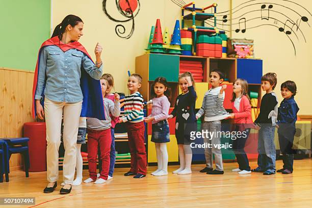 group of children playing with their teacher in kindergarten - preschool classroom stockfoto's en -beelden