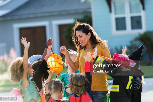 woman giving out candy to children trick or treating - boy fireman costume stock pictures, royalty-free photos & images