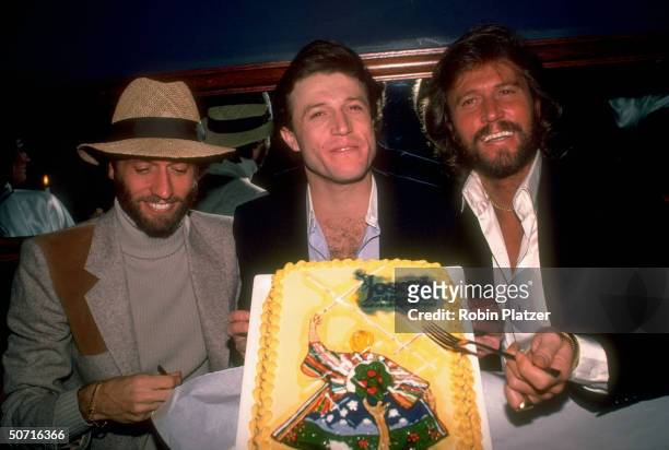 Singer Andy Gibb with brothers Barry and Maurice holding a cake emblazoned with Joseph and the Amazing Technicolor Dreamcoat logo during time Andy...