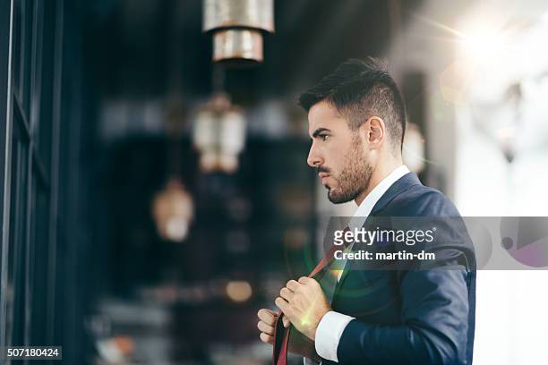 businessman getting dressed in front of the mirror - adjusting necktie stockfoto's en -beelden
