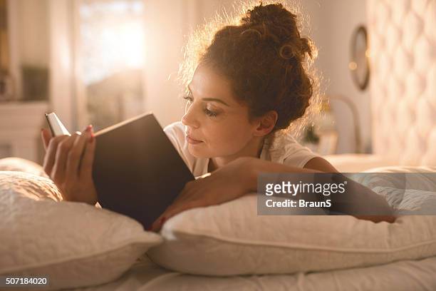 relaxed woman reading a book in her bed. - reading stockfoto's en -beelden