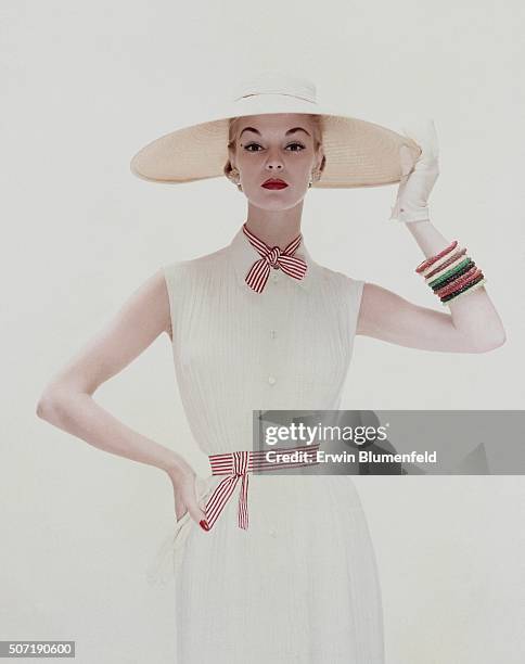 Model wearing white tucked crepe dress, of Dacron and rayon, tied with red and white stripes, by David Crystal; the hat, a wide circle of straw...