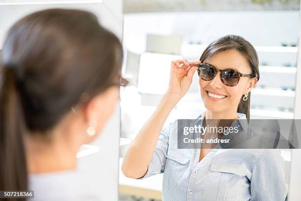 donna che compra occhiali da sole nel negozio dell'ottico - sunglasses foto e immagini stock