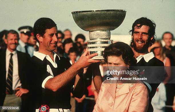 Queen Elizabeth II makes a funny face as Prince Charles holds a trophy above her head following a polo match at Windsor Great Park on July 01, 1984...