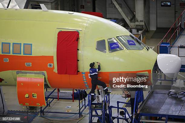 Worker stands on a raised platform to inspect the exterior fuselage skin of a Sukhoi Superjet 100 aircraft during construction at the Sukhoi Civil...