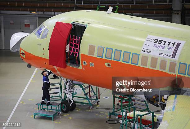 Worker uses an access panel beneath the cockpit to fit systems to a Sukhoi Superjet 100 aircraft during construction at the Sukhoi Civil Aircraft Co....