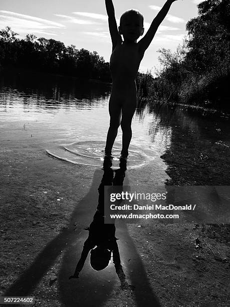 toddler frolics in shallow river with silhouettes, shadows, and reflections - skinny dipping kids stock-fotos und bilder