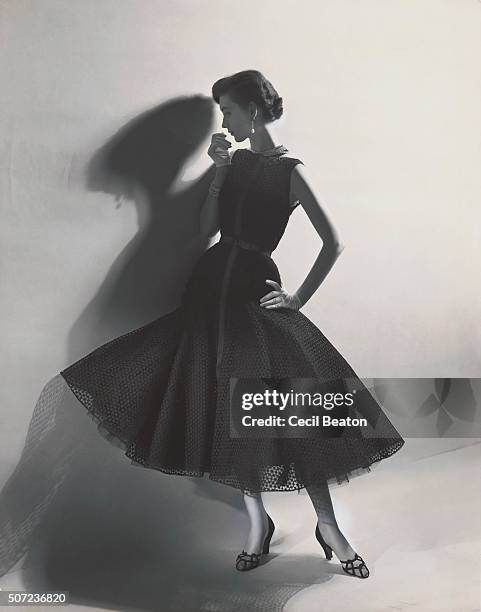 Model wearing a sleeveless black eyelet dress with flared skirt by Mainbocher, with Harry Winston diamond bracelet, necklace and earrings.