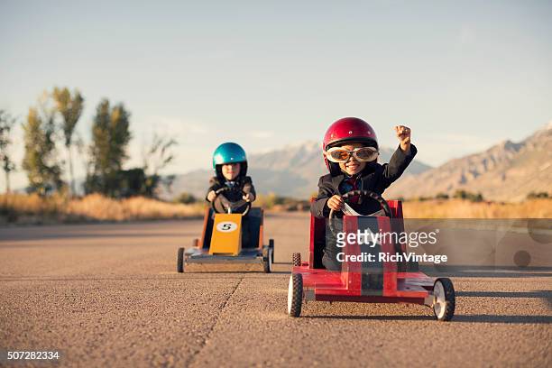 junge business-jungen in anzügen rennen spielzeug-autos - motivation stock-fotos und bilder