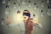 Blindfolded woman walking through lightbulbs searching bright idea