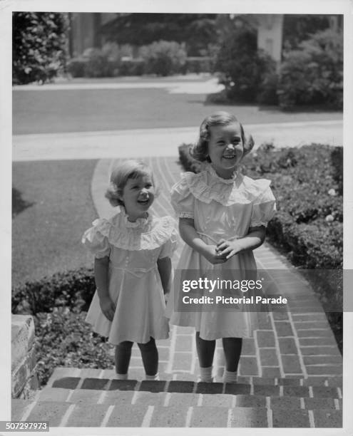 The daughter of actor Errol Flynn, Arnella Roma and Deirdre, wearing matching dress on the front steps of a house, circa 1955.