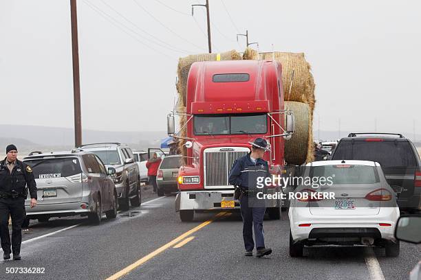 An Oregon State Police officer and a Washington County Sheriff deputy help guide a truck and trailer hauling hay through a narrow gap of media...