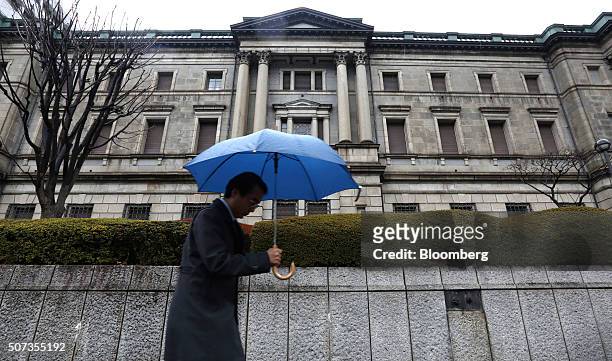 Pedestrian holding an umbrella walks past the Bank of Japan headquarters in Tokyo, Japan, on Friday, Jan. 29, 2016. Haruhiko Kuroda, BOJ governor,...