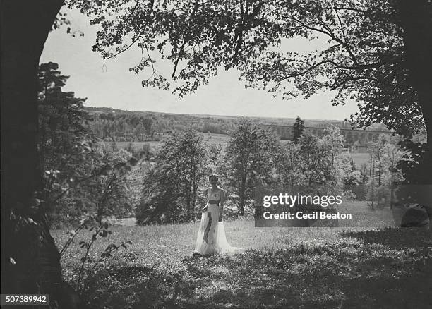 The Duchess of Windsor, standing in the gardens of the Chateau de Cande, wearing a long white sleeveless dress with a hand-painted lobster motif on...