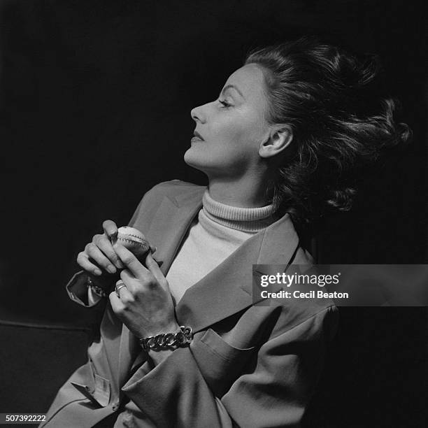 Upper half of Actress Greta Garbo recumbent on sofa with head turned and hair streaming down; She wears a light tailored jacket with a white...