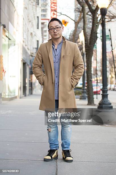 Allen Brewer is seen on Oak Street wearing Warby Parker glasses, camel wool J Lindeberg coat, blue/white fine checker Public School shirt, torn blue...