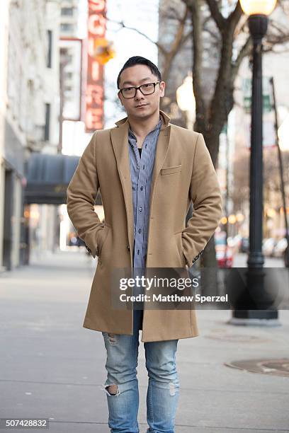 Allen Brewer is seen on Oak Street wearing Warby Parker glasses, camel wool J Lindeberg coat, blue/white fine checker Public School shirt, torn blue...