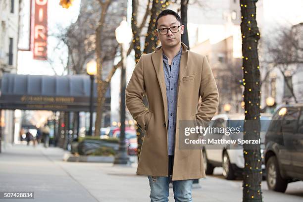 Allen Brewer is seen on Oak Street wearing Warby Parker glasses, camel wool J Lindeberg coat, blue/white fine checker Public School shirt, torn blue...