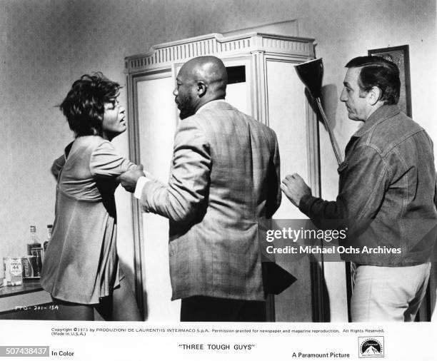 Isaac Hayes roughly questions Paula Kelly as Lino Ventura stand as backup in a scene from the Paramount Pictures movie "Three Tough Guys", circa 1974.