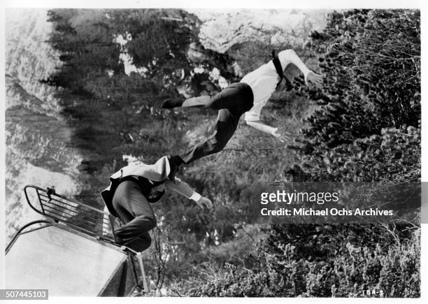 David McCallum and Domenico Modugno fall of a ski lift after their fight in a scene from the MGM movie "Three Bites of the Apple", circa 1967.
