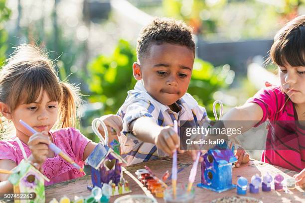 multi-ethnic children painting bird houses outdoors - bird feeder stockfoto's en -beelden