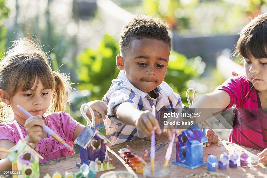 Multi-ethnic children painting bird houses outdoors