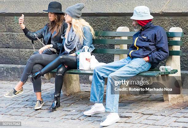 Generation Gap on everyday New York scene.Young girls take a selfie seated in a bench in the streets of New York while a senior man watches.