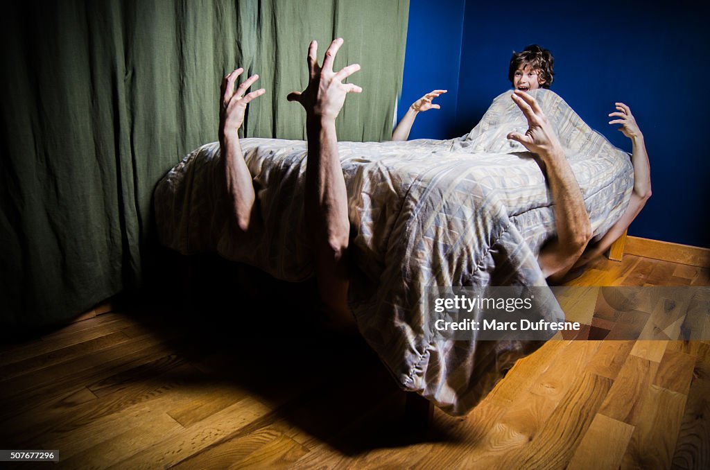 Young boy hiding in bed with monsters under bed