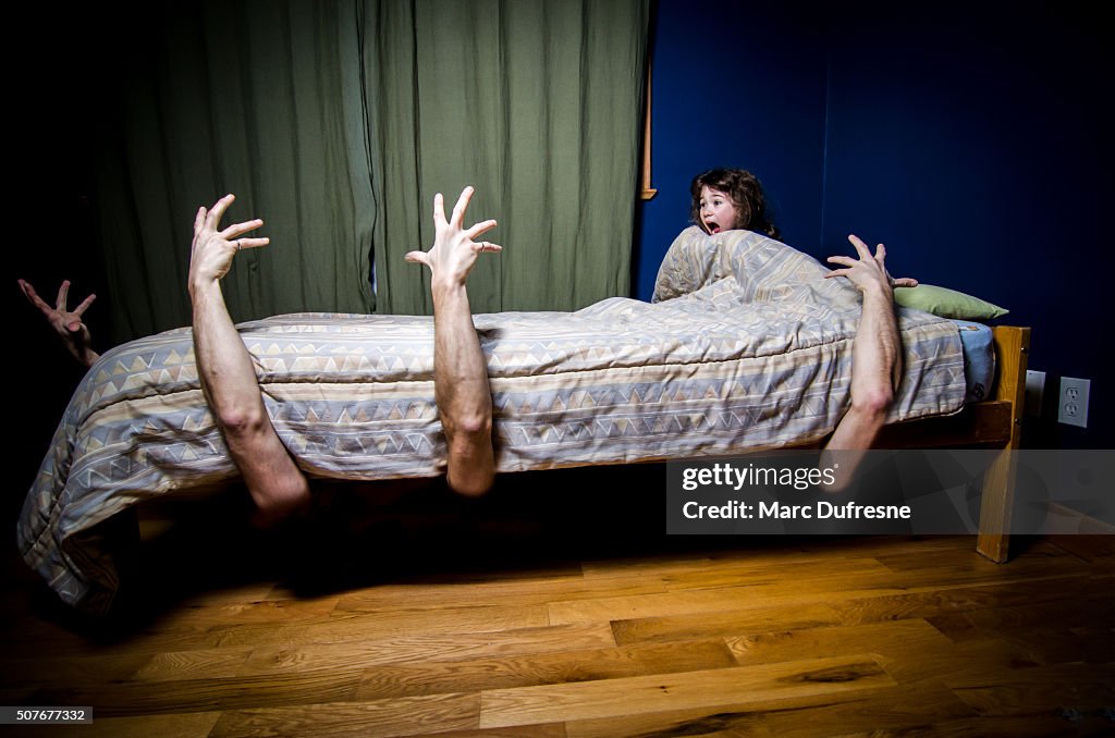 Young girl hiding in bed with monsters under bed