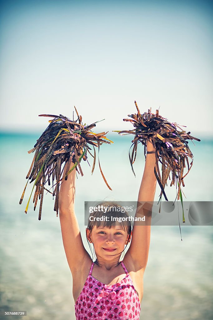 Little cheerleader playing with seaweed on the beach