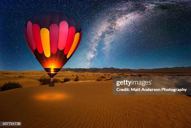a majestic hot air balloon soars under the stars of the milky way, over the desert - mesquite dunes of death valley national park. moonlight provides luminosity showing the patterns and shapes of the desert landscape. - heteluchtballon stockfoto's en -beelden