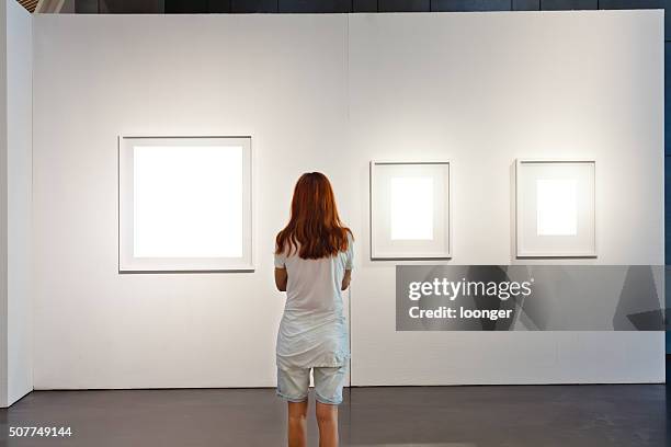 one woman looking at white frames in an art gallery - photo exhibition stock pictures, royalty-free photos & images