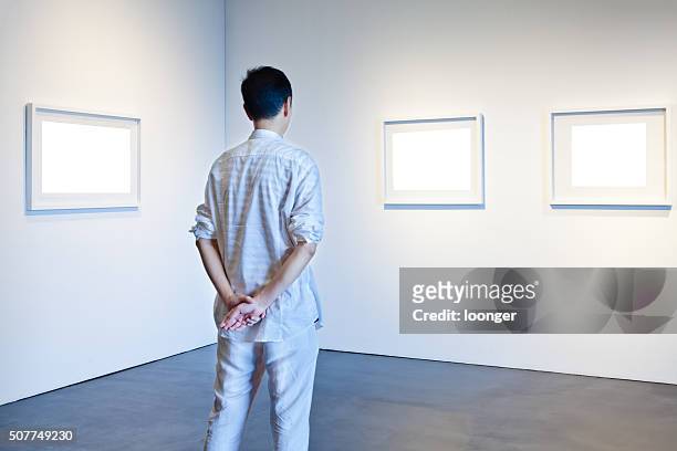 one man looking at white frames in an art gallery - art museum stockfoto's en -beelden
