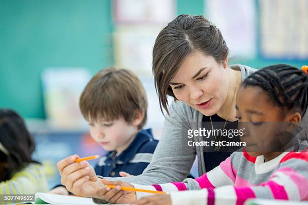 teacher helping a student understand an assignment - elementary school building stock pictures, royalty-free photos & images