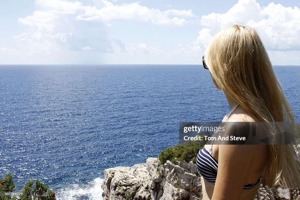 Blonde tourist girl looks out over vast sea