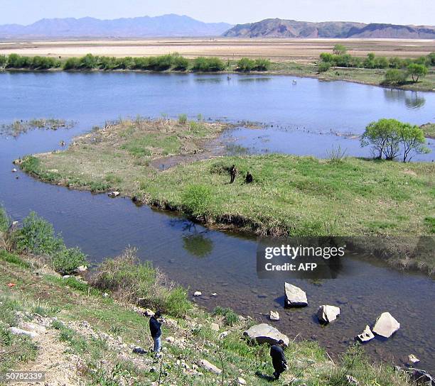 Narrow strip of the Yalu River divides China and North Korea, where two guards wait at the border of their poverty-stricken country from a patch of...