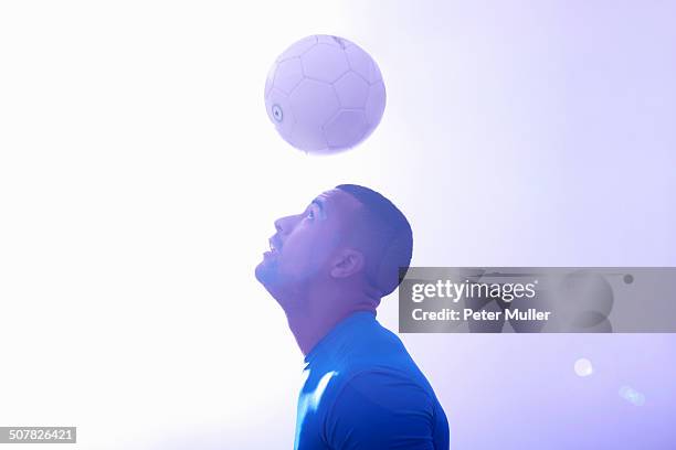 studio shot of young male soccer player keeping ball mid air with header - faire une tête photos et images de collection