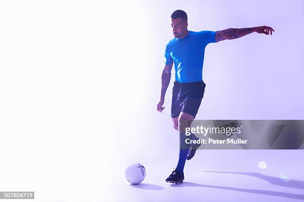 studio shot of young male soccer player kicking the ball - treten stock-fotos und bilder