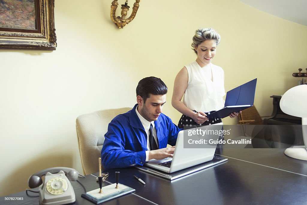 Young vintage couple at desk with files and laptop