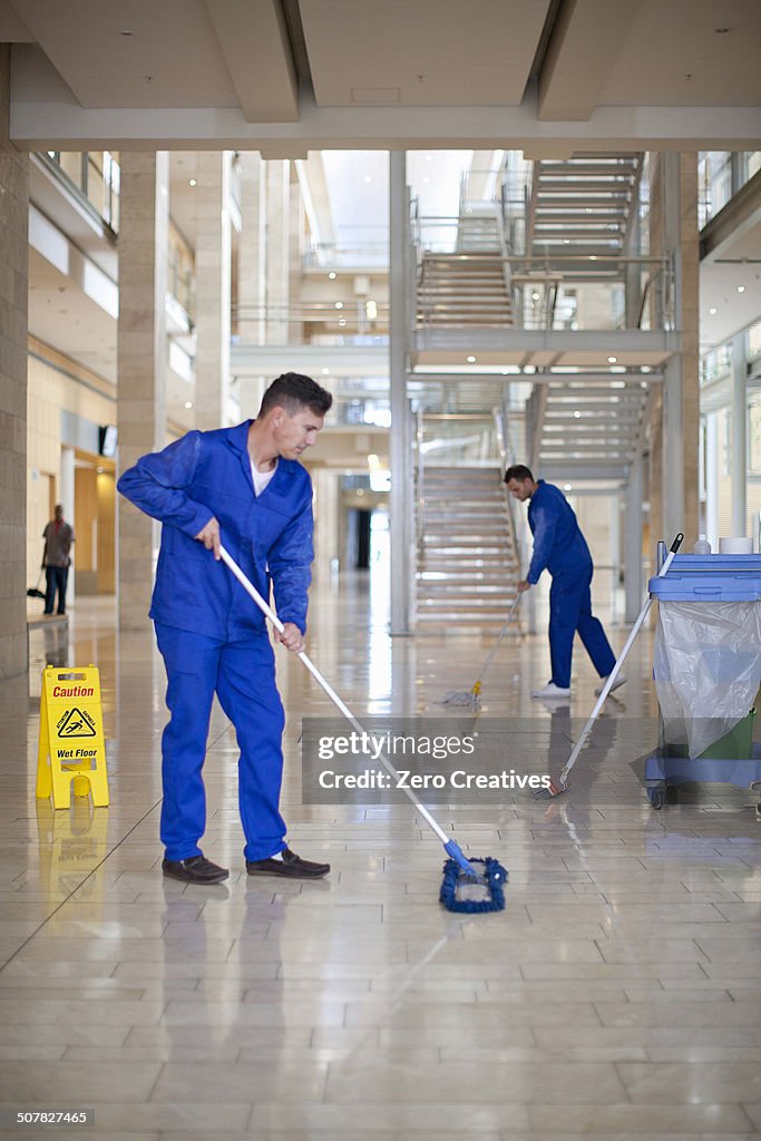 Male cleaners mopping in office atrium