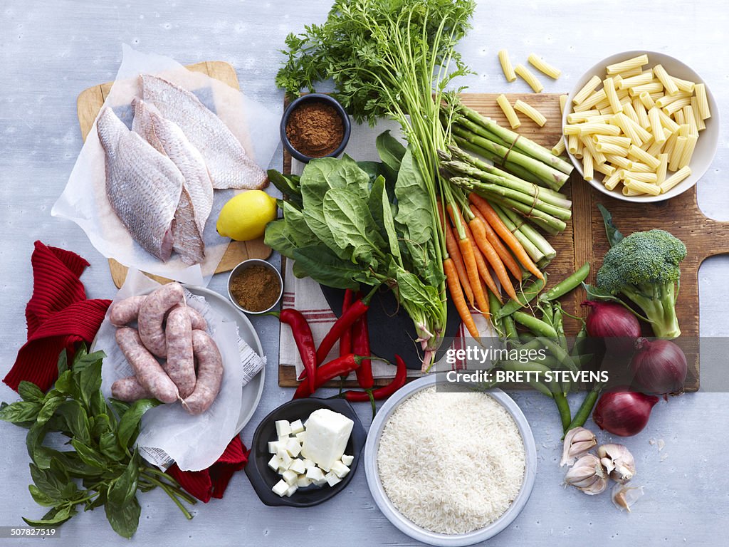 Overhead view of fish, pork sausage, feta and selection of fresh organic herbs and vegetable