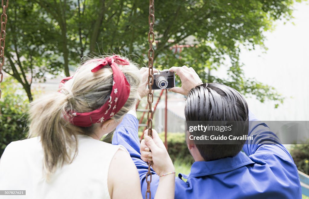 Rear view of young vintage couple taking selfie with camera in garden