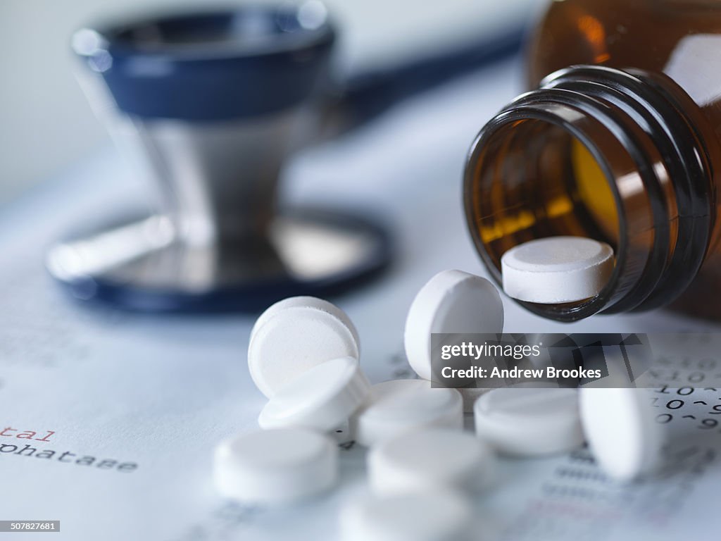 Close up of stethoscope and pain killers pouring onto medical test results