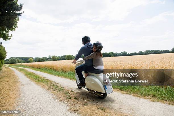 rear view of mature man and daughter riding motor scooter along dirt track - moped stock-fotos und bilder