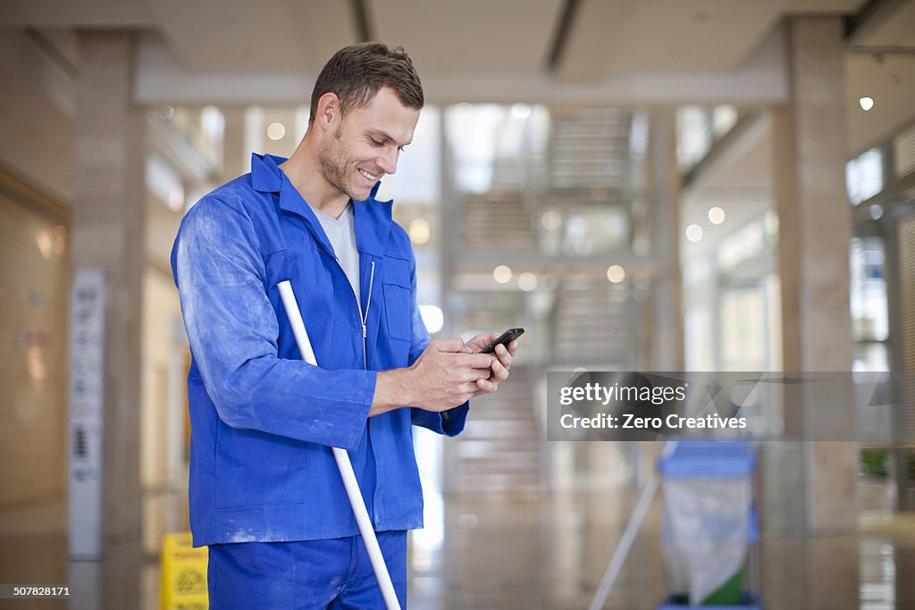 Male cleaner texting on smartphone in office atrium