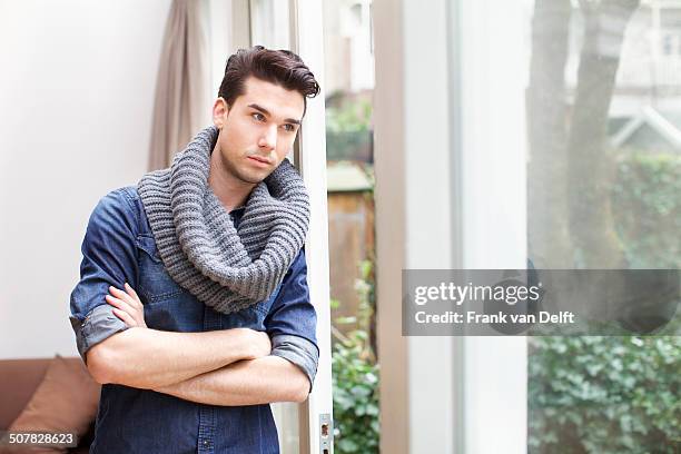 young man gazing out of window in living room - snood headwear stock pictures, royalty-free photos & images