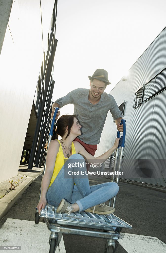 Young couple fooling around on shopping cart in street