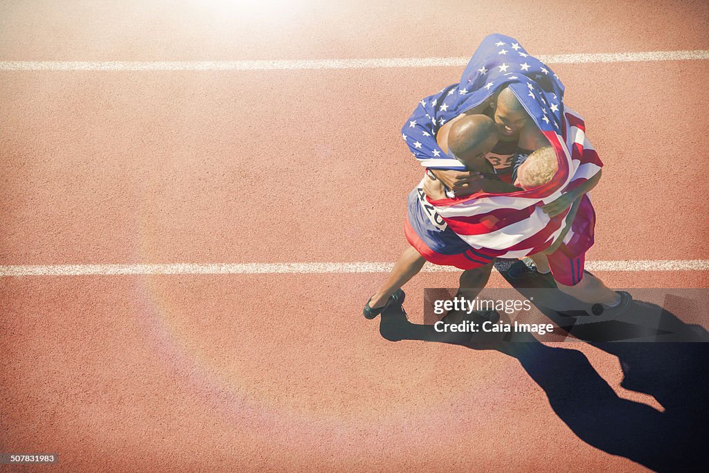 Runners wrapped in American flag hugging on track