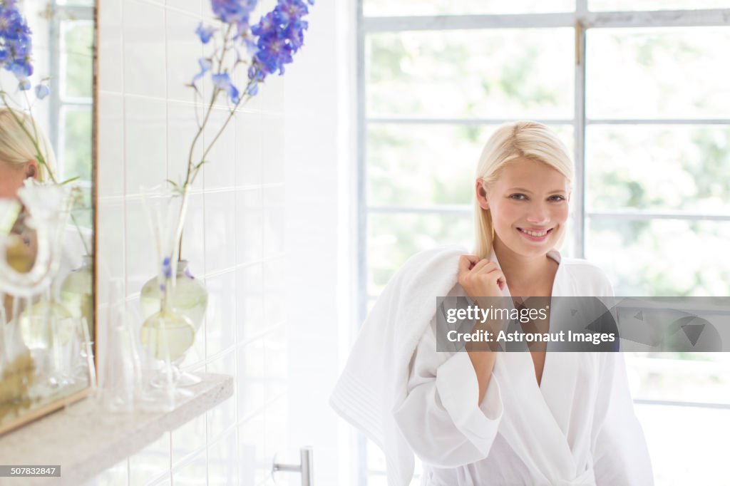 Woman in bathrobe smiling in bathroom